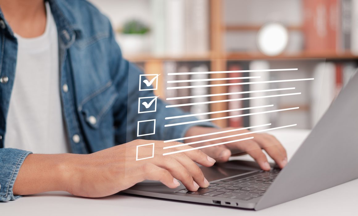 Woman in jean jacket from the neck down working on a silver laptop doing an IRS WISP review for her tax firm.